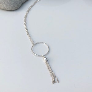 May include: A silver necklace with a circle pendant and a chain tassel.