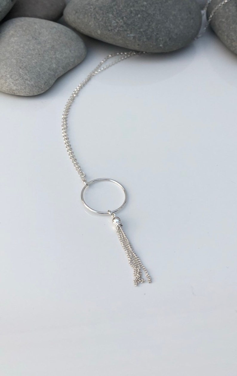 May include: A silver necklace with a circle pendant and a chain tassel.
