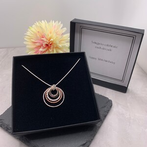 May include: A silver necklace with a pendant of five interlocking circles in silver, rose gold, and gold. The necklace is in a black box with a white card that reads "5 rings to celebrate each decade. Happy 50th birthday."