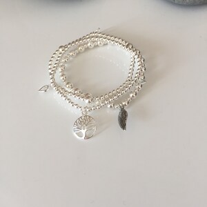May include: Three silver beaded bracelets with charms, including a tree of life and a wing charm.