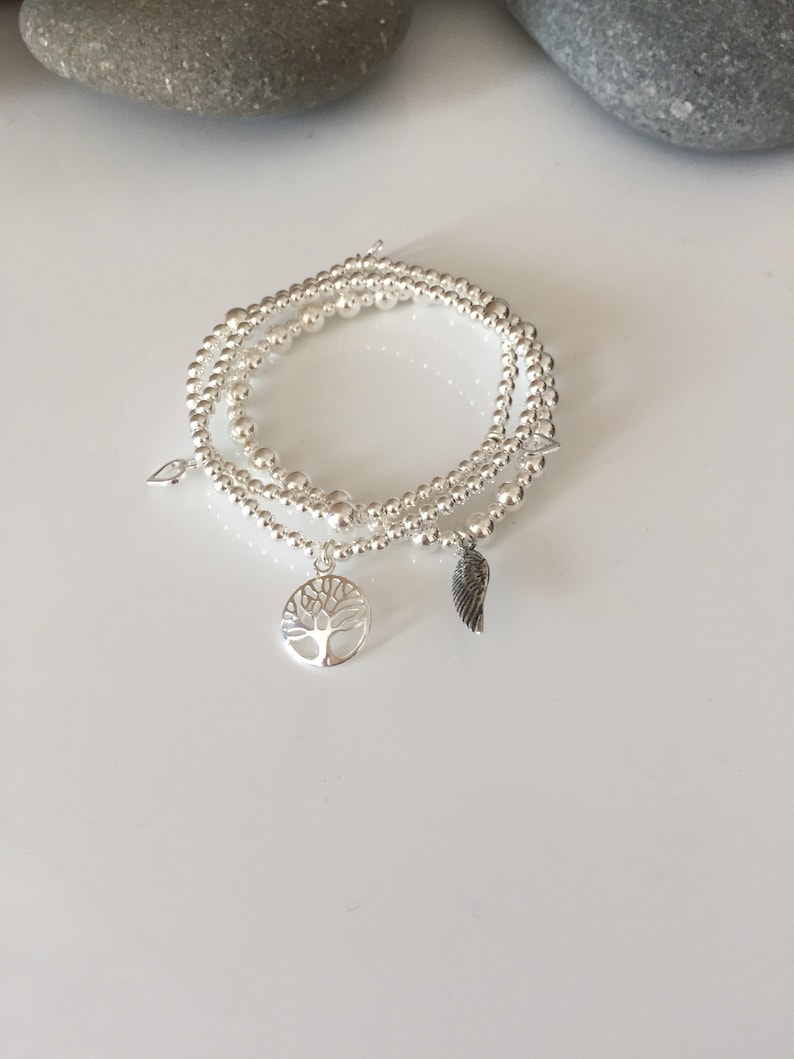 May include: Three silver beaded bracelets with charms, including a tree of life and a wing charm.