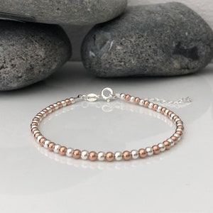 May include: A silver and rose gold beaded bracelet with a lobster clasp closure.