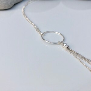 May include: A silver necklace with a circle pendant and a tassel chain.