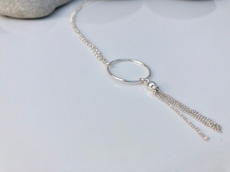 May include: A silver necklace with a circle pendant and a tassel chain.