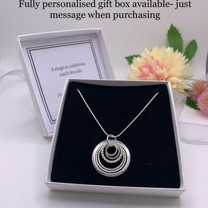 Pu&ograve; includere: Una collana d'argento con un ciondolo a sei cerchi intrecciati, presentata in una scatola regalo bianca con interno nero. La scatola contiene un biglietto all'interno che recita "6 anelli per celebrare ogni decennio".