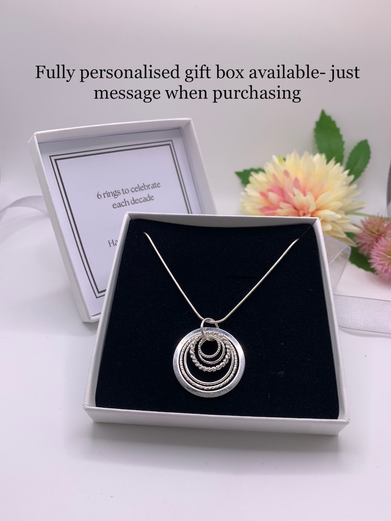 Pu&ograve; includere: Una collana d'argento con un ciondolo a sei cerchi intrecciati, presentata in una scatola regalo bianca con interno nero. La scatola contiene un biglietto all'interno che recita "6 anelli per celebrare ogni decennio".