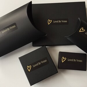 May include: Four black boxes with gold hearts and the text "Loved By Venus" on them. The boxes are different sizes and shapes.