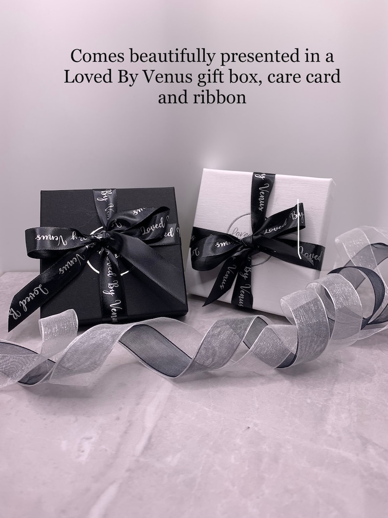 May include: Two gift boxes with black ribbon and the words "Loved By Venus" printed on them. The boxes are sitting on a white surface with a white and black ribbon.
