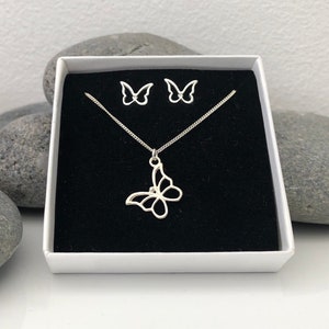 May include: A silver butterfly necklace and matching stud earrings set displayed in a white gift box with a black velvet interior. The butterfly pendant and earrings have an openwork design.