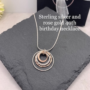 May include: Sterling silver and rose gold necklace with three interlocking circles. The necklace is on a black slate surface.  "Sterling silver and rose gold 40th birthday necklace" is written in white text on a black background.