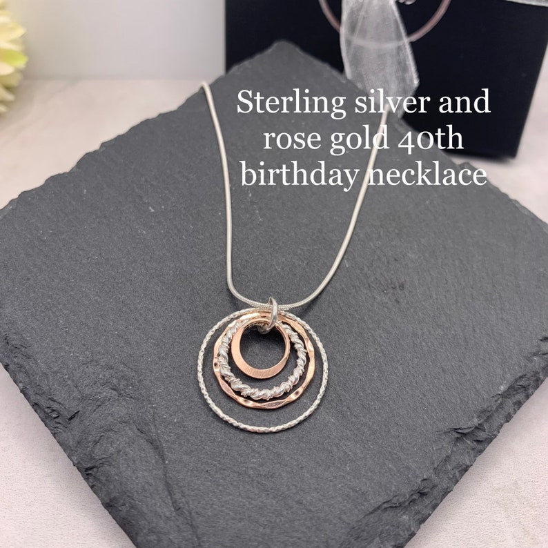 May include: Sterling silver and rose gold necklace with three interlocking circles. The necklace is on a black slate surface.  "Sterling silver and rose gold 40th birthday necklace" is written in white text on a black background.