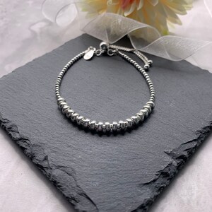 A silver beaded bracelet with a sliding clasp. The bracelet is on a black slate surface.