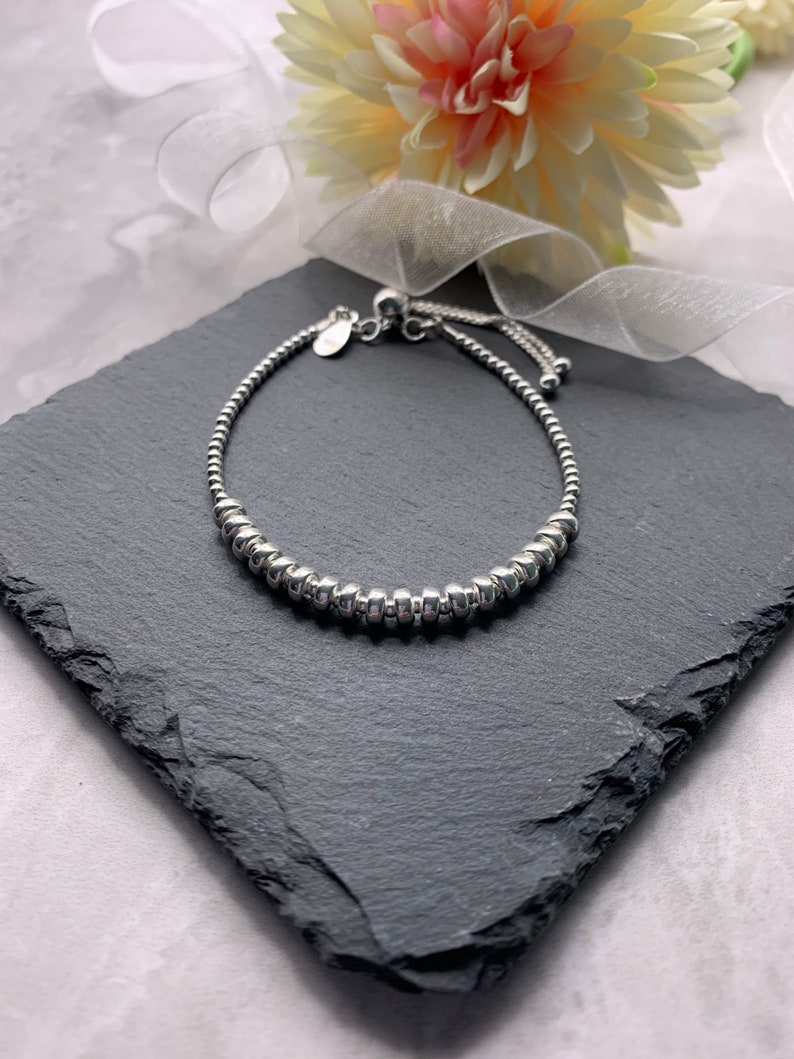 A silver beaded bracelet with a sliding clasp. The bracelet is on a black slate surface.