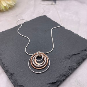 May include: A silver chain necklace with a pendant made of four interlocking circles. The circles are made of silver and rose gold, and they are arranged in a graduated size.