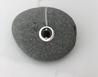 May include: A silver necklace with a round pendant featuring a black lava rock bead inside a circle.