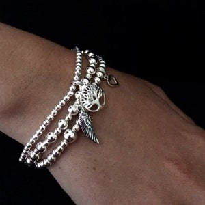 May include: A silver bracelet with three strands of beads and three charms: a tree, a heart, and a wing.