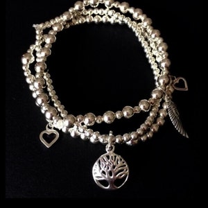 May include: Three silver beaded bracelets with charms. The charms include a tree of life, a heart, and a feather.