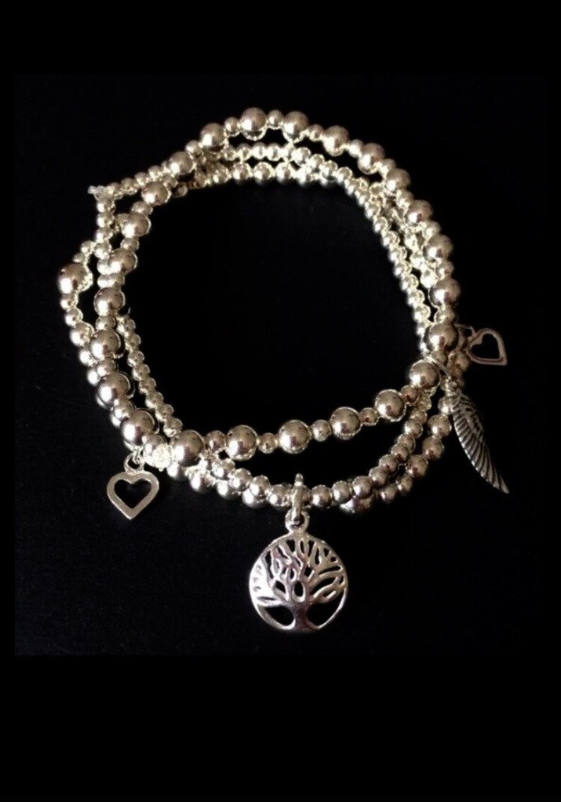 May include: Three silver beaded bracelets with charms. The charms include a tree of life, a heart, and a feather.