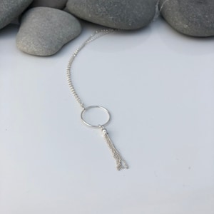 May include: A silver necklace with a circle pendant and a chain tassel.