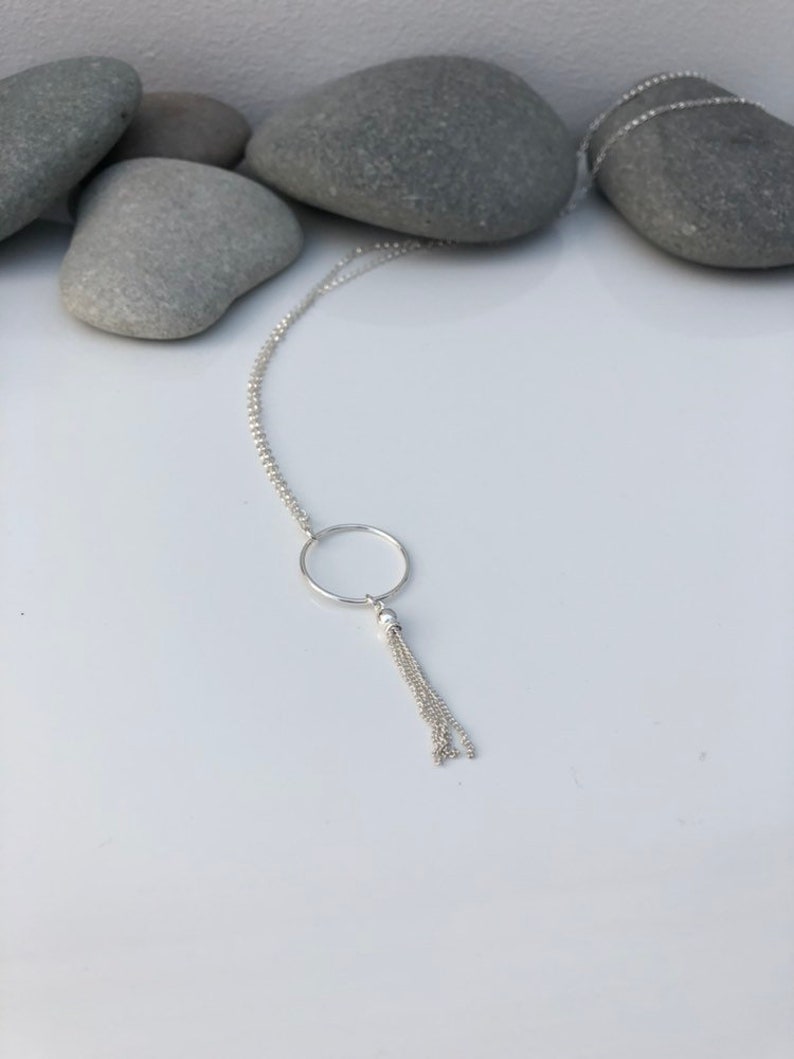 May include: A silver necklace with a circle pendant and a chain tassel.