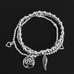 May include: Three silver beaded bracelets with charms. The charms are a heart, a tree of life, and a wing.