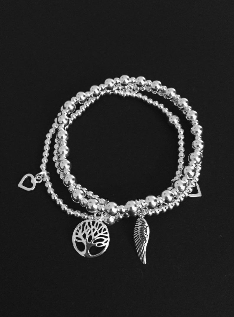 May include: Three silver beaded bracelets with charms. The charms are a heart, a tree of life, and a wing.