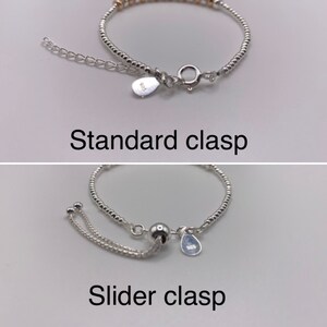 May include: Two silver bracelets with different clasps. The top bracelet has a standard clasp with a small silver tag. The bottom bracelet has a slider clasp with a small silver tag.
