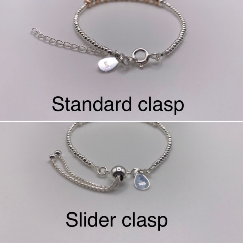 May include: Two silver bracelets with different clasps. The top bracelet has a standard clasp with a small silver tag. The bottom bracelet has a slider clasp with a small silver tag.