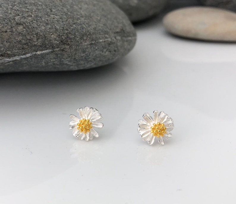 K&ouml;nnte beinhalten: Ein Paar silberne Daisy-Ohrstecker mit goldenen Zentren. Die Ohrringe sind klein und zart, perfekt f&uuml;r den Alltag.