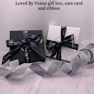 Puede incluir: Dos cajas de regalo, una negra y otra blanca, con una cinta negra y blanca. Ambas cajas tienen el texto "Loved By Venus" impreso.