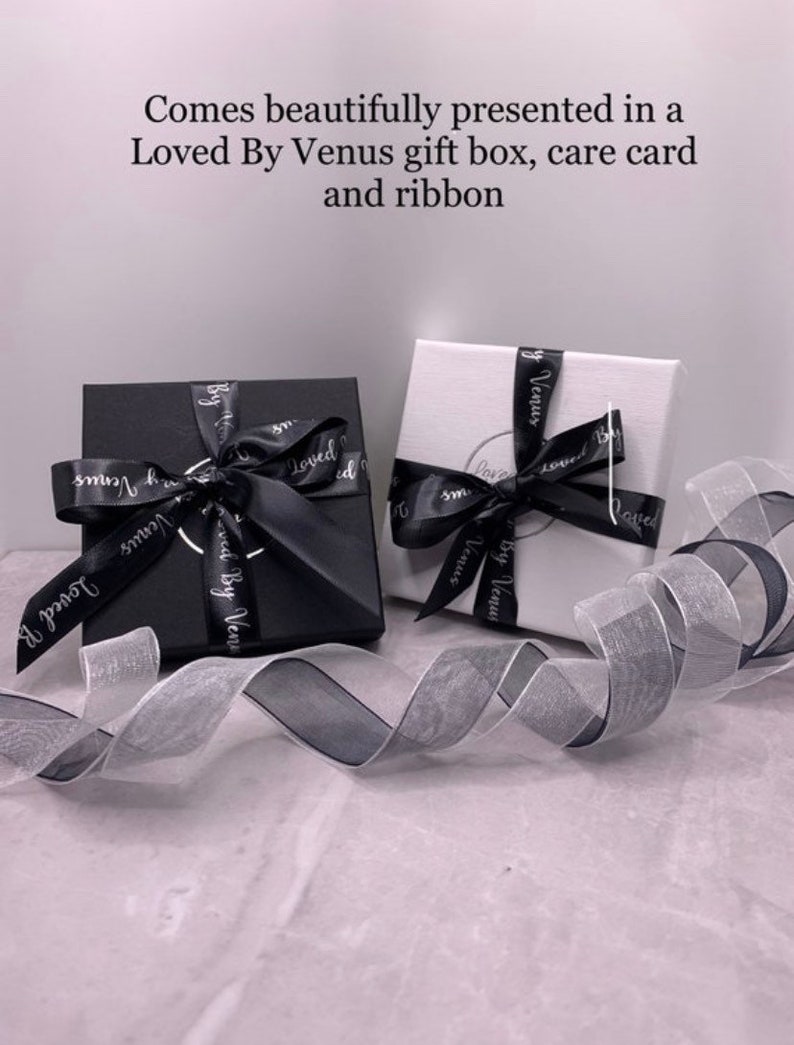 Puede incluir: Dos cajas de regalo, una negra y otra blanca, con una cinta negra y blanca. Ambas cajas tienen el texto "Loved By Venus" impreso.