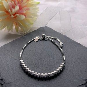 A silver beaded bracelet with a sliding clasp. The bracelet is on a black slate surface.