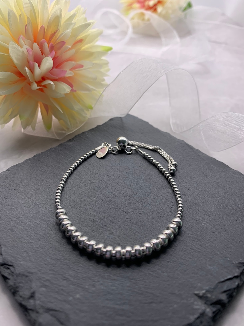 A silver beaded bracelet with a sliding clasp. The bracelet is on a black slate surface.