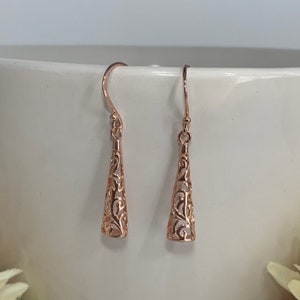 May include: A pair of rose gold filigree dangle earrings. The earrings are made of a delicate, intricate design with a cone shape.