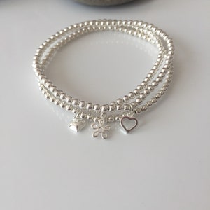 May include: Three silver beaded bracelets with charms. The charms are a small heart, a flower, and a larger heart with an open centre.