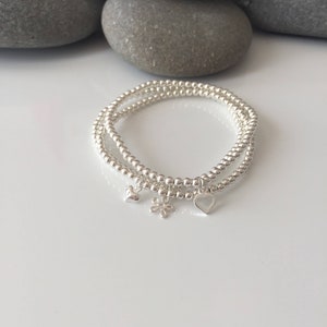 May include: Two silver beaded bracelets with charms. The charms are a small heart, a larger heart with an open centre, and a flower.