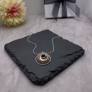 May include: A silver chain necklace with a pendant made of three interlocking circles. The circles are silver, rose gold, and silver, and they are textured.