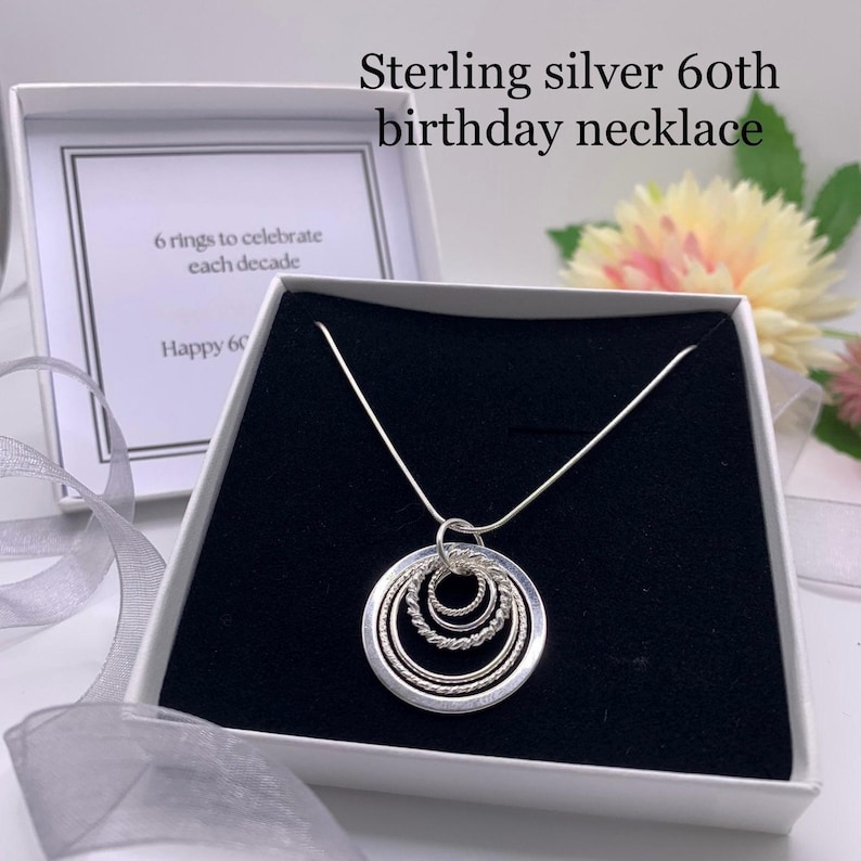Pu&ograve; includere: Collana in argento sterling con sei cerchi intrecciati, un regalo per un 60&deg; compleanno. La collana &egrave; in una scatola bianca con un biglietto che dice "6 anelli per celebrare ogni decennio" e "Buon 60".