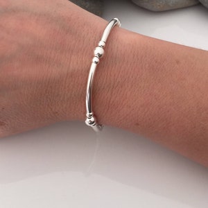 Puede incluir: Un brazalete de plata con tres peque&ntilde;as cuentas redondas.