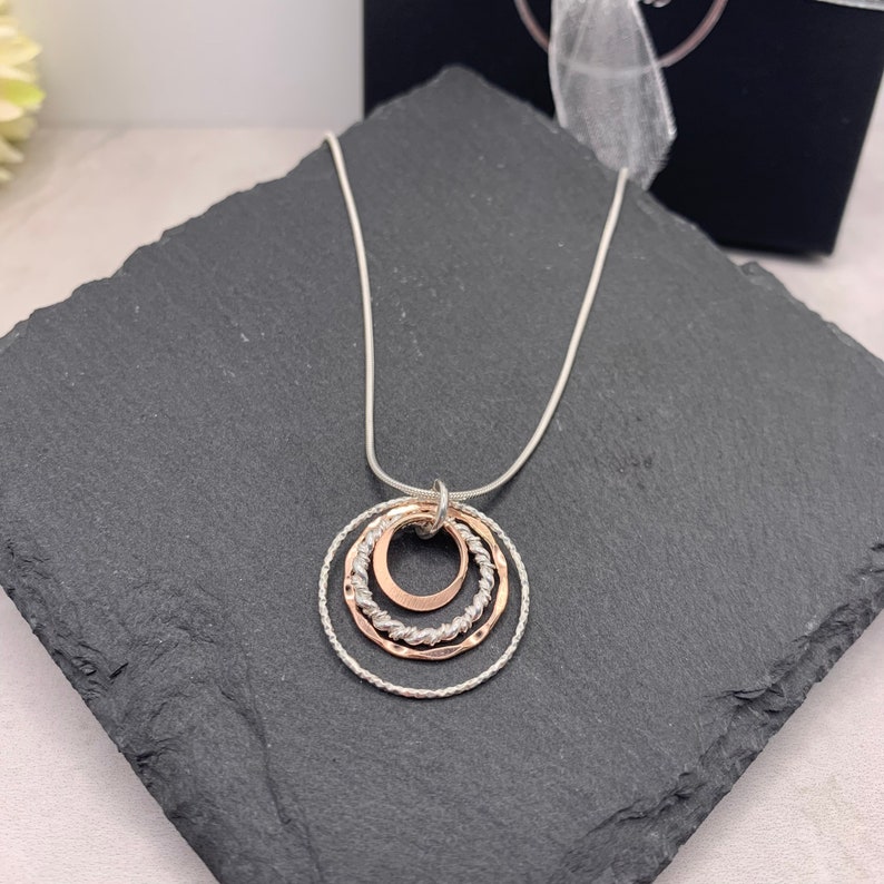 May include: A silver chain necklace with a pendant featuring three interlocking circles. The outer two circles are silver, and the inner circle is rose gold.