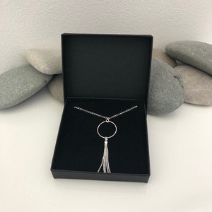 May include: A silver necklace with a circle pendant and a tassel. The necklace is in a black box.