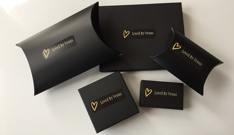 May include: Five black boxes with gold hearts and the text "Loved By Venus" on them. The boxes are different sizes and shapes.