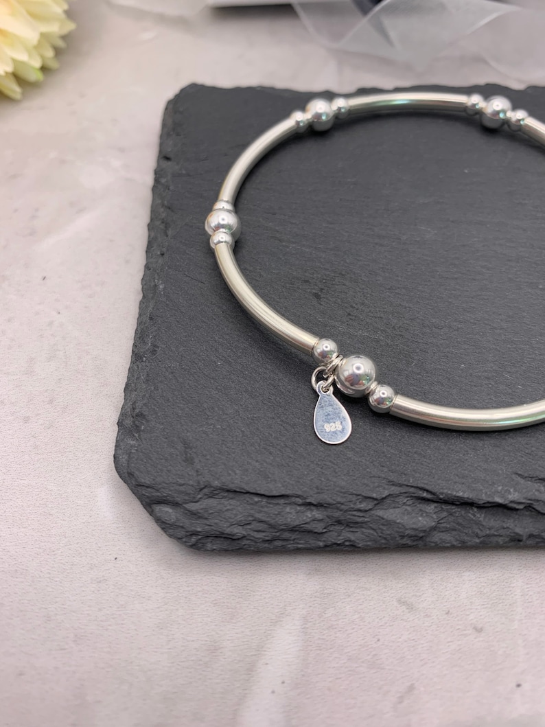 Puede incluir: Una pulsera de plata con un dije que dice "925". La pulsera tiene una serie de peque&ntilde;as cuentas de plata.