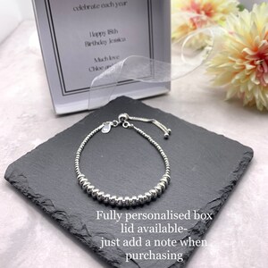 A silver beaded bracelet with a sliding clasp. The bracelet is on a black slate surface. The text "Fully personalised box lid available - just add a note when purchasing" is below the bracelet.