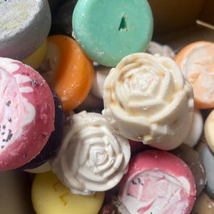 May include: A selection of colourful, round soaps. Some are solid colours like green, orange, and yellow. Others have a marbled effect in pink and white. Several soaps are shaped like roses, and some have a small hole in the top.