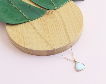 May include: A delicate gold chain necklace with a triangular opal pendant. The opal is a milky white colour with a subtle shimmer.