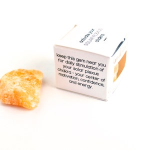 May include: A small, orange crystal with a white box that reads "activate your solar plexus chakra - keep this gem near you for daily stimulation of your solar plexus chakra - your center of motivation, confidence, and energy."