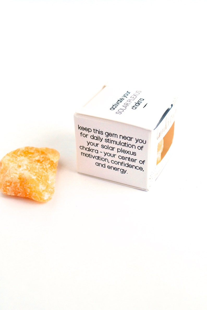 May include: A small, orange crystal with a white box that reads "activate your solar plexus chakra - keep this gem near you for daily stimulation of your solar plexus chakra - your center of motivation, confidence, and energy."