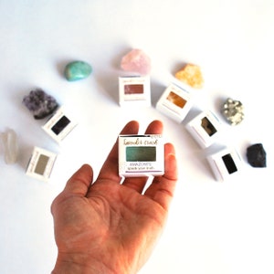 K&ouml;nnte beinhalten: Eine kleine, quadratische, wei&szlig;e Schachtel mit einem gr&uuml;nen Lidschatten darin. Die Schachtel tr&auml;gt den Text "lavende'r crush" und "AMAZONITE speak your truth".