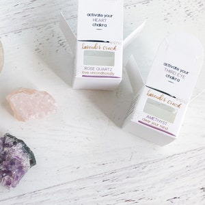 May include: Two white boxes with lavender crush written on them. The boxes contain crystals and are labeled with the chakra they are associated with. The top box is labeled "activate your heart chakra" and contains rose quartz. The bottom box is labeled "activate your third eye chakra" and contains amethyst.
